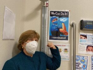 CSUN alumna Terri Stratton, ’78 (Health Science), MPH ’85 (Public Health), the chief executive officer of El Dorado Community Health Centers, poses with a COVID-19 vaccine poster.