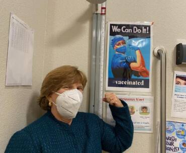 CSUN alumna Terri Stratton, ’78 (Health Science), MPH ’85 (Public Health), the chief executive officer of El Dorado Community Health Centers, poses with a COVID-19 vaccine poster.
