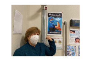CSUN alumna Terri Stratton, ’78 (Health Science), MPH ’85 (Public Health), the chief executive officer of El Dorado Community Health Centers, poses with a COVID-19 vaccine poster.