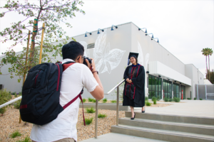 A graduating student in her cap and gown smiles for a photo on campus.