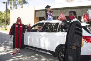 Beck and Watkins stand by a white SUV with a graduate standing out of the sunroof