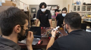 Students wearing masks sitting around a desk looking at cables.