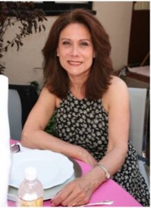 Annette Cardona is sitting at a table, smiling at the camera.