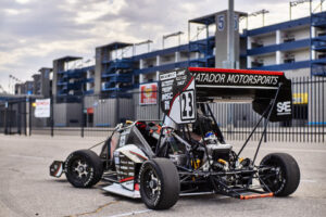 Small formula-style race car standing in the pavement against a building.
