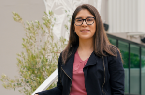 Erika Baron is standing up smiling at the camera with a building on the background.
