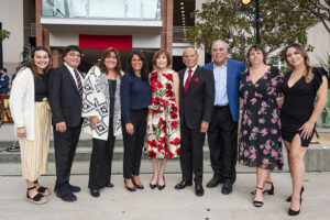 9 members of the Valera family pose for a group photo. They are standing and Valera Hall is in the background.