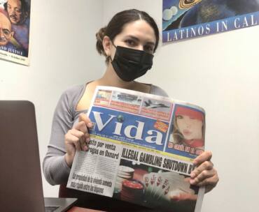 Daniela Torres is holding a newspaper that says "Vida" on the front.