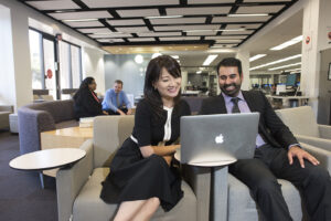 Nazarian College meet in the University Library's Learning Commons, sitting and looking at a laptop.