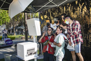 Students wearing large glasses stand in front of photo equipment on University Library lawn
