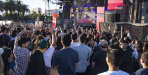 Students standing on University Library lawn in foreground. Rapper Blxst on stage in background.