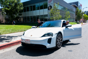White Porsche with one person on driver's side and one on passenger side admiring car.
