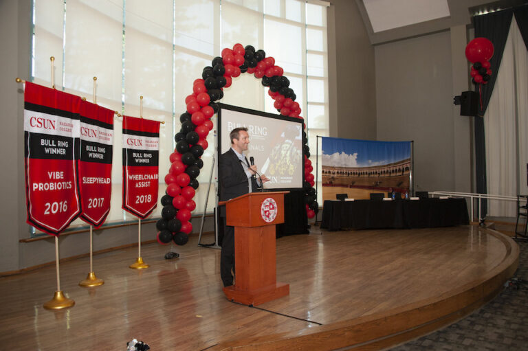 Arch made of balloons with a man in the center on a podium holding a microphone