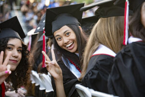 Graduates in caps and gowns smile and flash peace signs (or victory signs), at Commencement 2022.