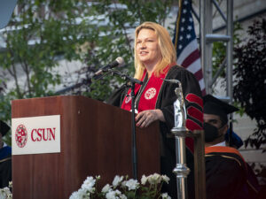 President Erika D. Beck, in black and red robes, stands behind a podium, speaking to the crowd at Honors Convocation 2022.