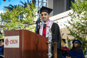 Associated Students President and graduate Jonathan Hay, in cap and gown, stands at a podium and speaks to the Class of 2022 at Commencement.