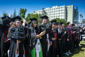 A row of graduates stand and move the tassels on their caps to the left, at Commencement 2022.
