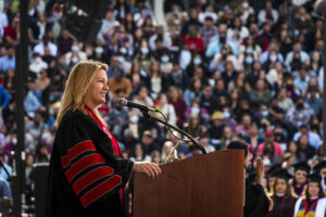 President Erika D. Beck, in red and black robes, stands at a podium on stage, in front of a large crowd, speaking at Commencement 2022.