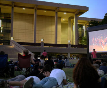 People sit on the lawn in front of the CSUN Library as a movie plays on a giant screen in the distance.