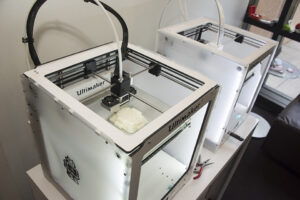Two 3D printers in the middle of printing out models.
