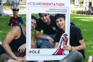 Three students pose for photo inside a white cardboard frame.