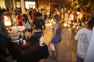 Two students in foreground stand front of buffet table holding plates.