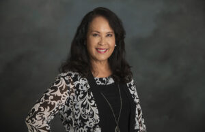 Horizontal, half-body shot of CSUN Alumni Association President Felicia Conlan, standing in front of a gray portrait background.