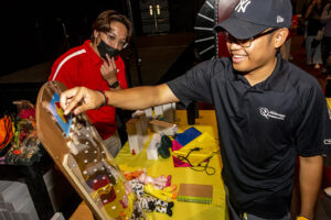Student stands playing game at table with person looking on.