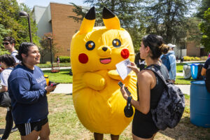 Person in bright yellow "Pikachu" costume stands with two students.