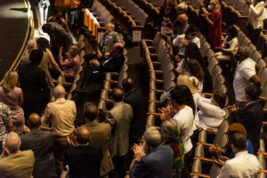 People in audience of theater stand in front of their seats in ovation.