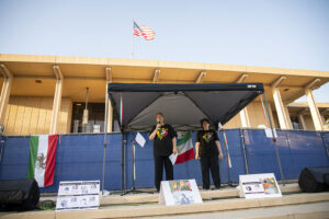 Two people stand under canopy in front of University Library, Iranian flag is off to the side.