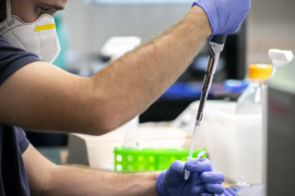 Scientist holding large syringe to be put into smaller sample sizes.