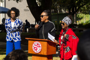 Dr. Barbara Rhodes speaks at the podium next to Dr. Marquita Gammage and Dr. Rehema Grey.