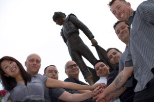 Students standing with hands put together in front of Matador statue.