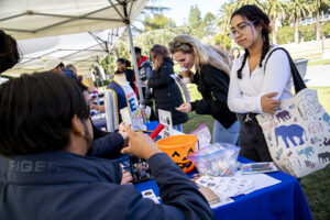 Two students stand at table talking to people seated. EOP shirt is on display in the background.