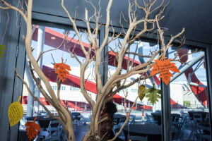 Small, bare-branched tree with paper leaves on it displayed in front of a window.