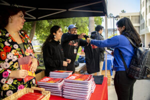 Table piled with red student planners, a student admires a black t-shirt.