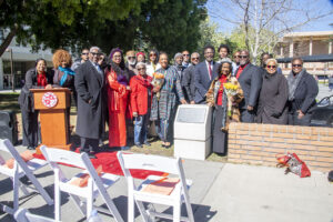 Group of people stand smiling behind plaque mounted on a concrete base.