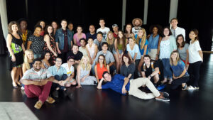Students standing and seated post for group photo. Megan Hilty is seated with students on floor.