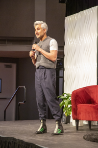 Tan France stands on stage with microphone.