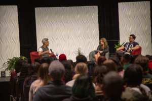 Tan France sits off to the left, Paige and Alex sit off to the right on stage at the USU