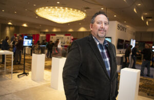 Andrew Elkins stands, looking into the camera, with the exhibit hall in the background