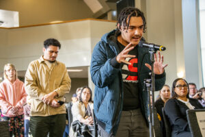 Students stands in front of microphone, asking Reverend Lawson a question, as other students stand behind them.