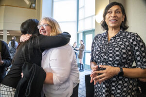 Two women hug while third woman looks at the camera.