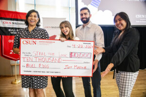Four people stand and smile for the camera while holding a giant check made out for $10,000.