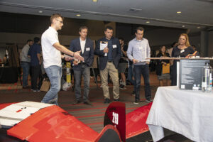 Student stands and gestures to wing of aircraft while judges stand beside him.