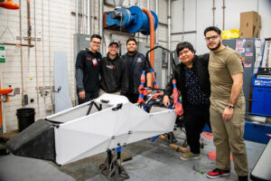Jacob Wright and four other team members stand around the body of their race car and smile for the photo.