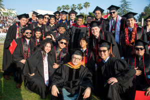 A group of students and professors in academic regalia stand together and pose for the camera