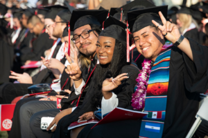 Smiling graduates in caps and gowns give the peace sign for the camera
