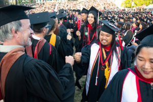 A line of graduates in caps and gowns greet each other.