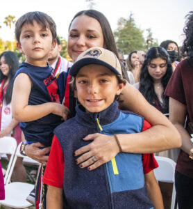 A mom and graduate holds one of her sons, and hugs the other, on the University Library lawn.